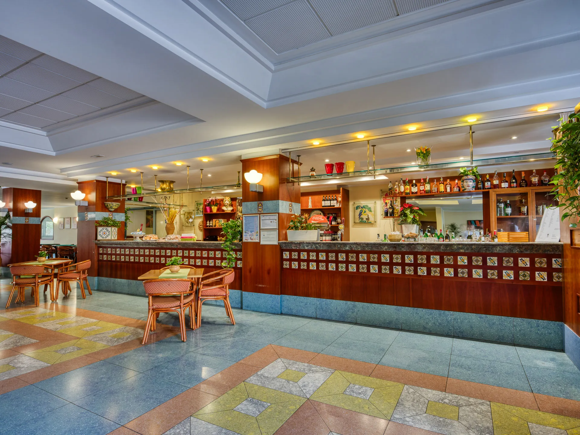 Hall dell'hotel con bancone bar in legno, piastrelle decorate e tavolini con sedie in rattan