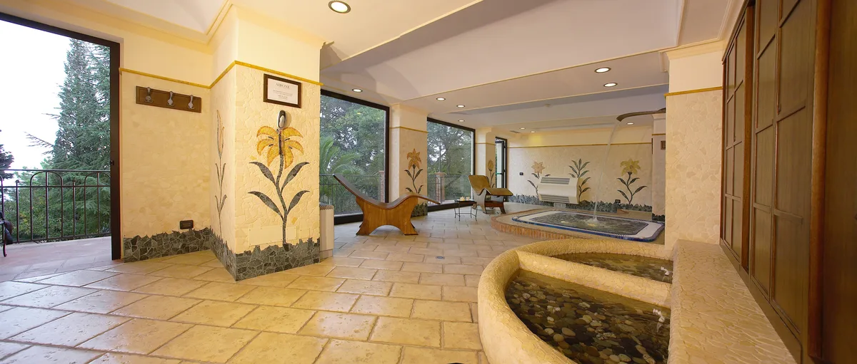 Area benessere con pavimento in pietra, fontane decorative e mosaici floreali con vista sul giardino