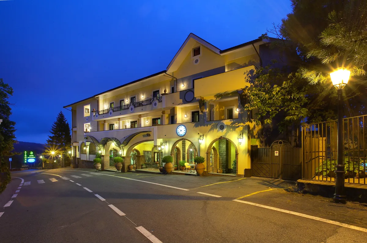 Facciata dell'hotel illuminata di notte con archi, orologio e lampioni