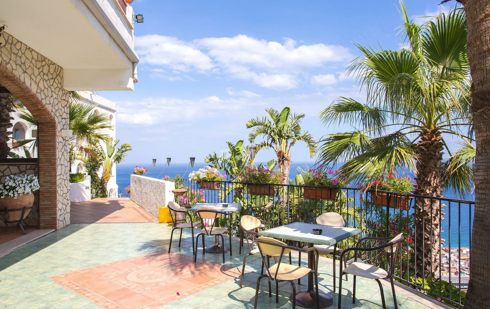 Terrazza con tavoli, palme e fiori affacciata sul mare