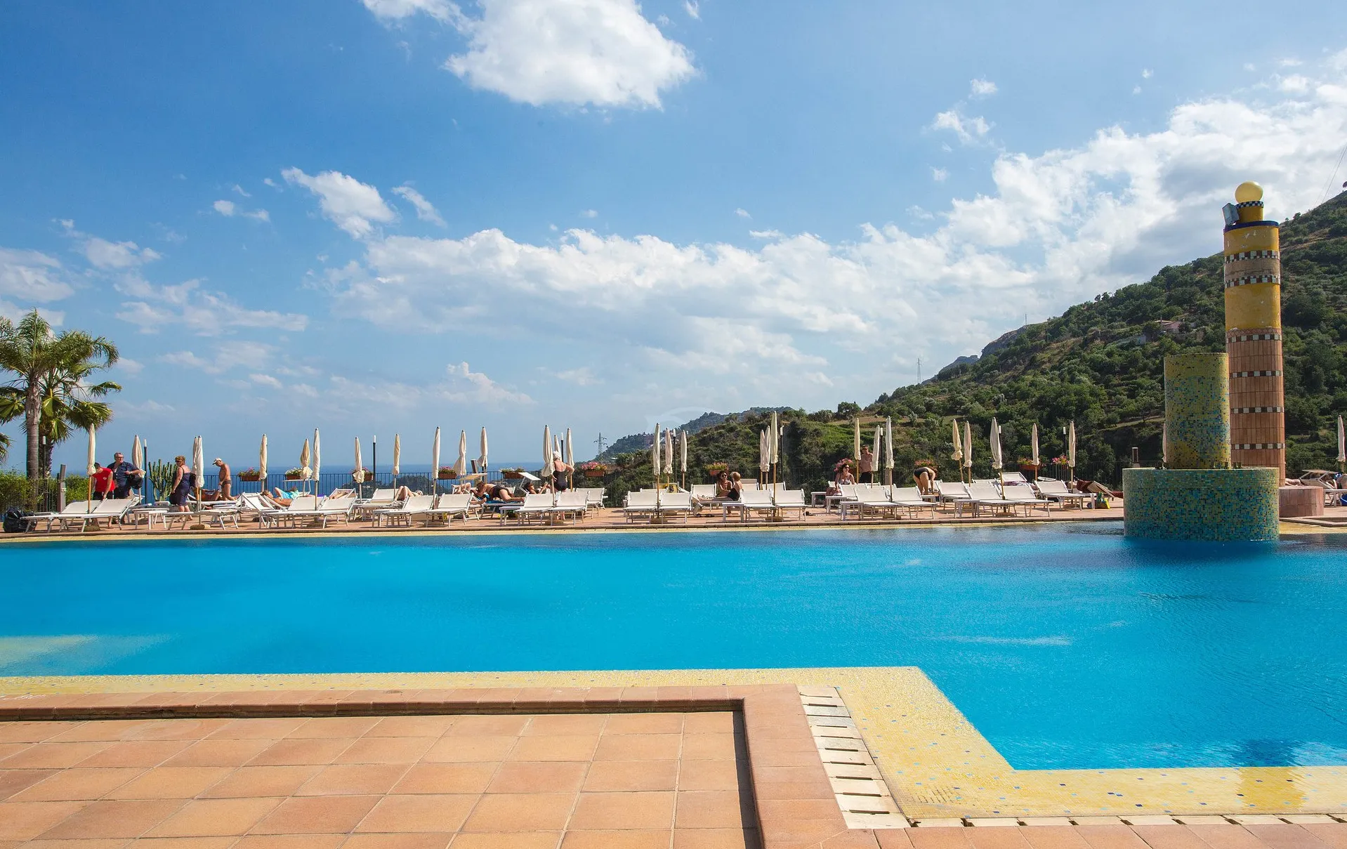 Piscina panoramica con lettini bianchi e ombrelloni chiusi affacciata sulle colline