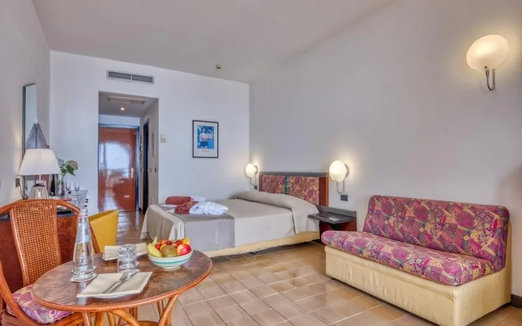 Camera dell'hotel con letto matrimoniale, divano e tavolino con frutta