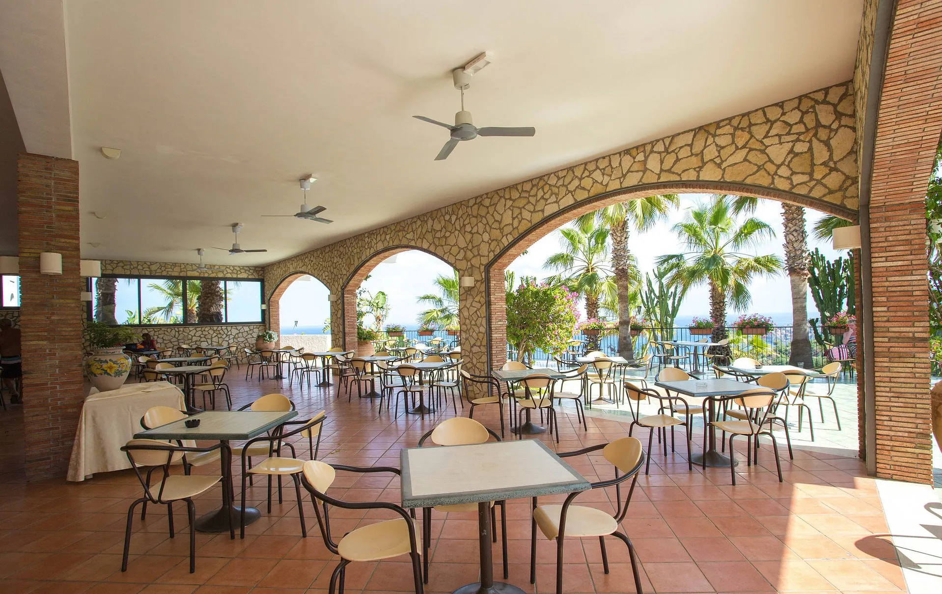 Ampia veranda con archi in pietra, tavoli e ventilatori affacciata sul mare