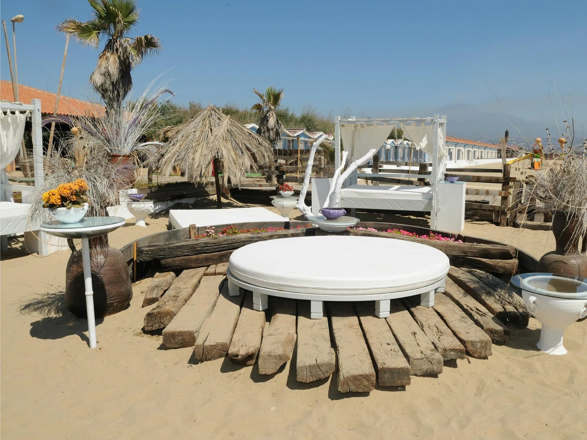 Zona relax sulla spiaggia con lettini bianchi e decorazioni floreali