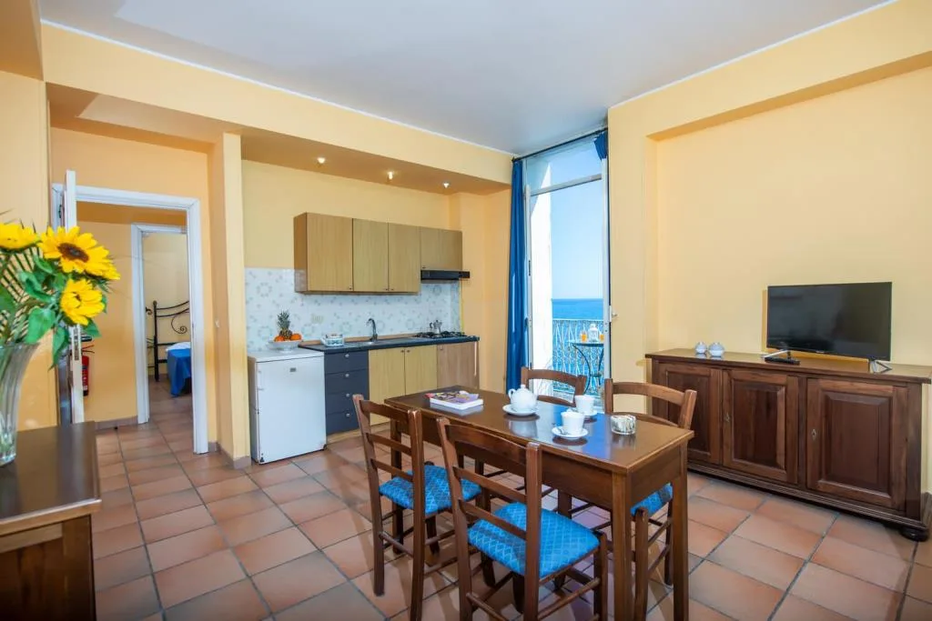 Soggiorno appartamento con angolo cottura, tavolo e vista mare dal balcone