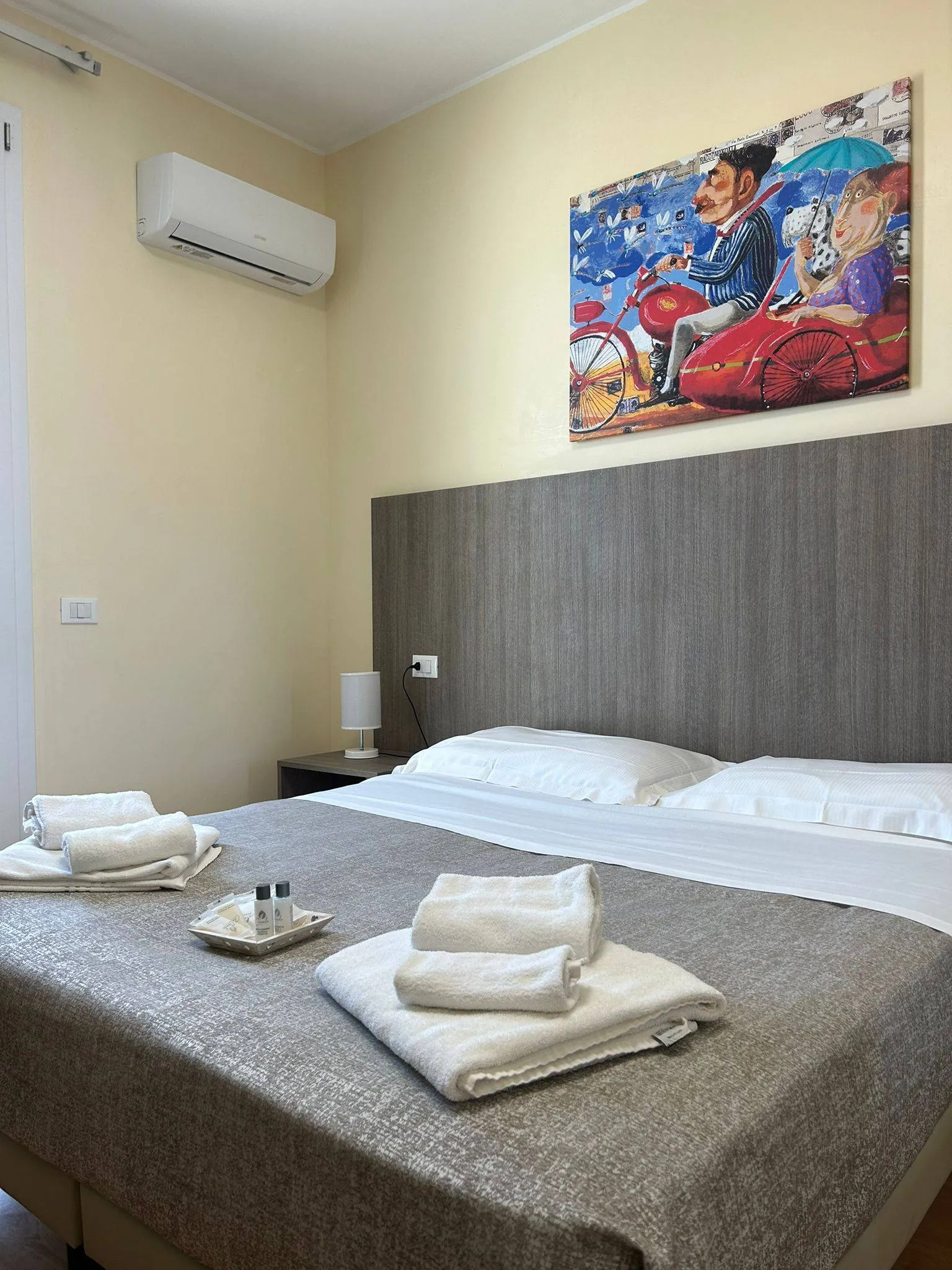 Camera matrimoniale con testiera in legno, quadro colorato, aria condizionata e asciugamani sul letto