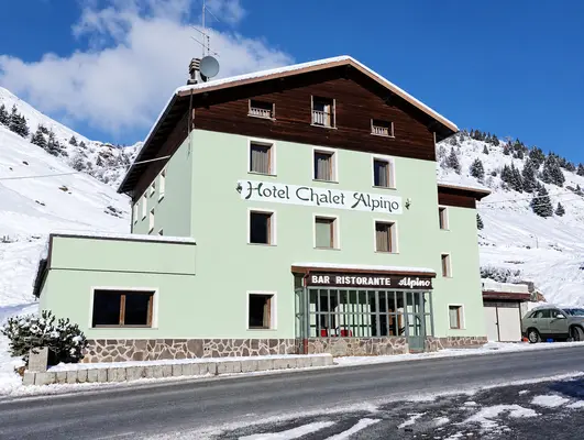 Facciata dell'Hotel Chalet Alpino con insegna e bar ristorante lungo la strada in inverno