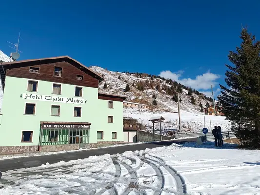 Esterno dell'Hotel Chalet Alpino con strada e montagna innevata sotto cielo azzurro