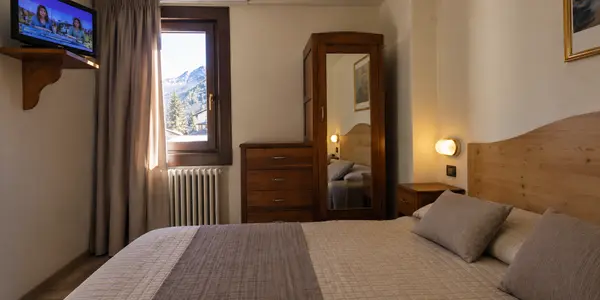 Camera da letto con letto matrimoniale, TV, cassettiera in legno e vista sulle montagne