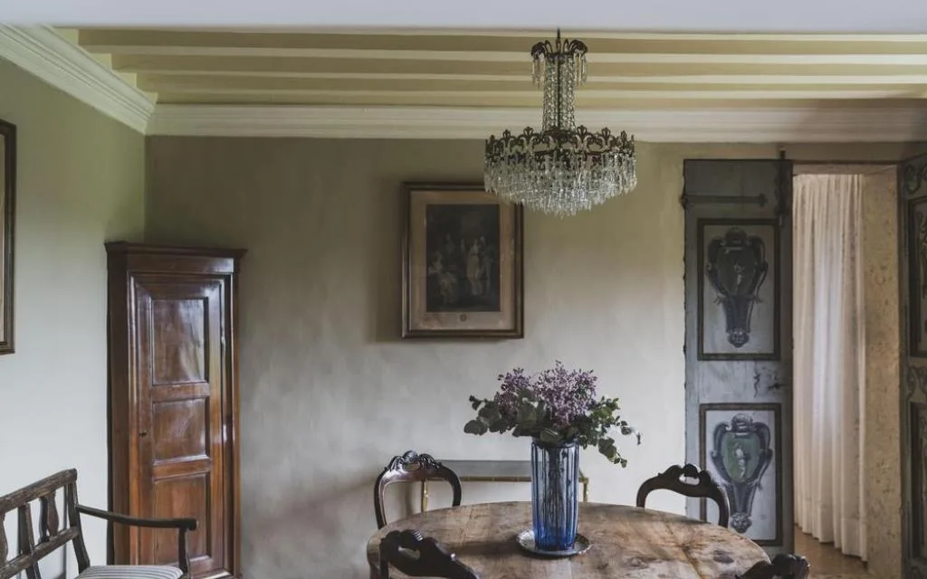 Sala da pranzo d'epoca con tavolo rotondo in legno, lampadario di cristallo e decori alle pareti
