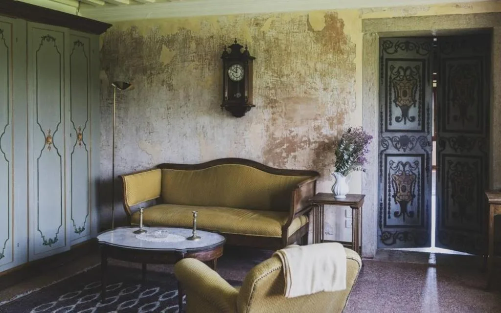Salotto rustico con divano vintage, orologio a parete e porta affrescata