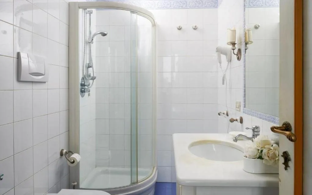 Bagno bianco con doccia curva in vetro e lavabo con specchio