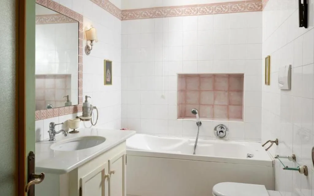 Bagno classico con vasca, lavabo e piastrelle bianche con bordo rosa