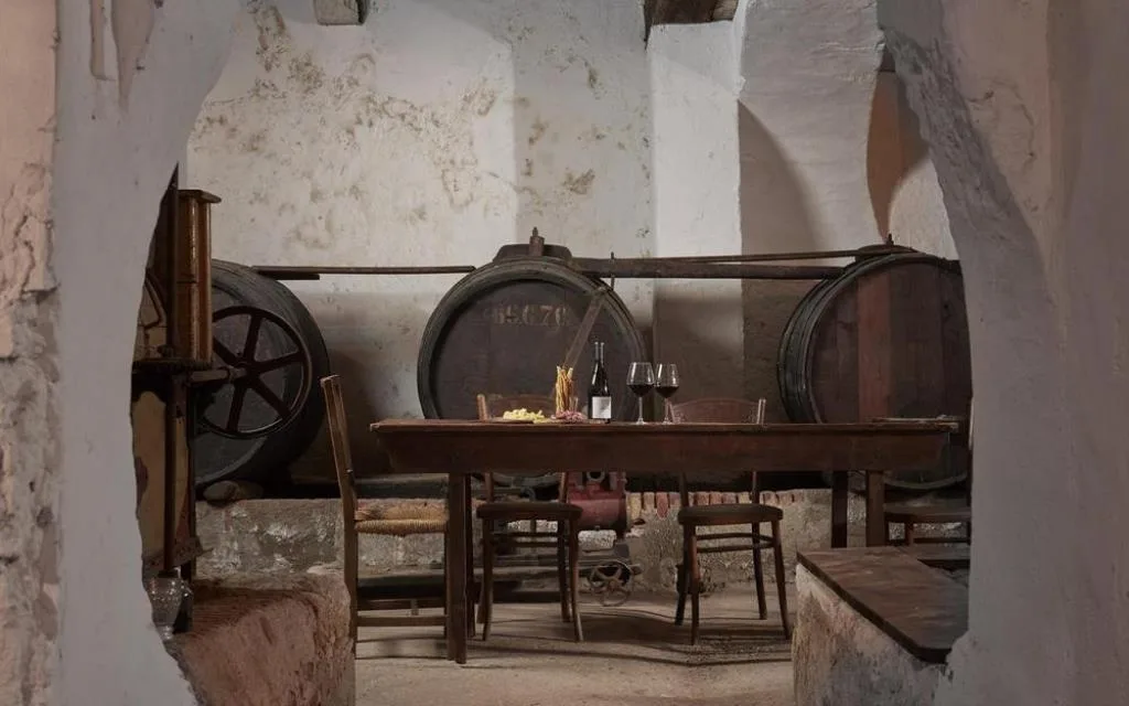 Cantina rustica con botti in legno, tavolo apparecchiato e vino rosso nei calici