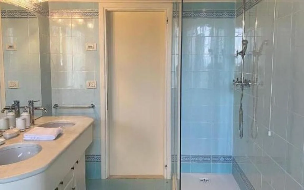 Bagno con piastrelle azzurre, doppio lavabo e doccia con vetro