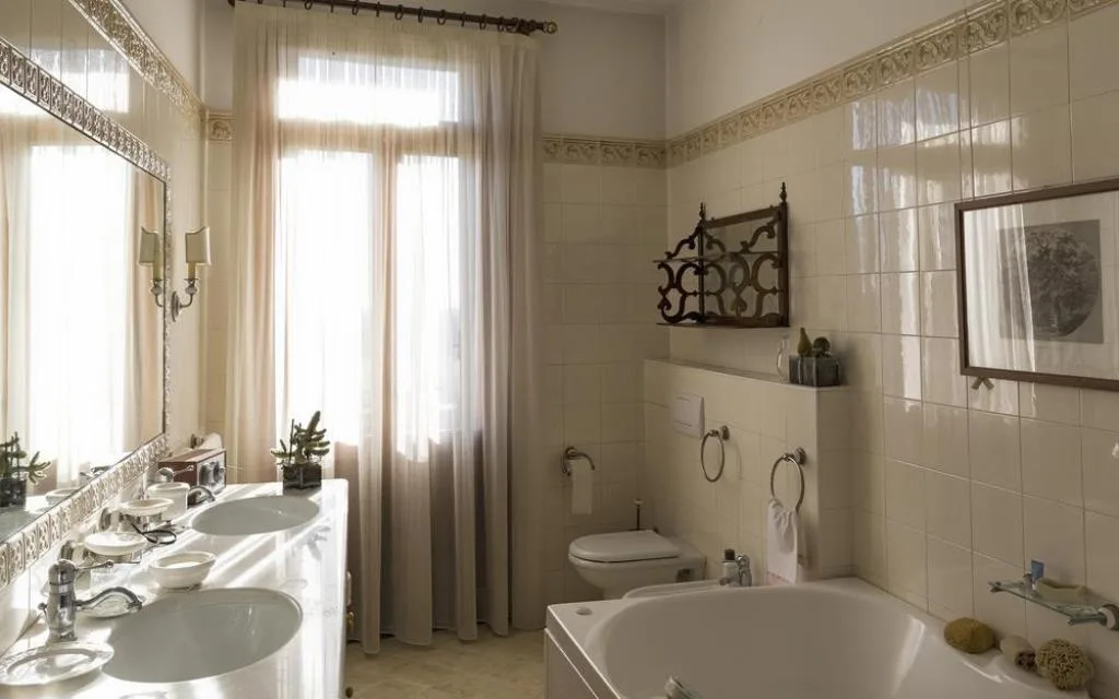 Bagno luminoso con vasca, doppio lavabo in marmo e tende chiare alla finestra