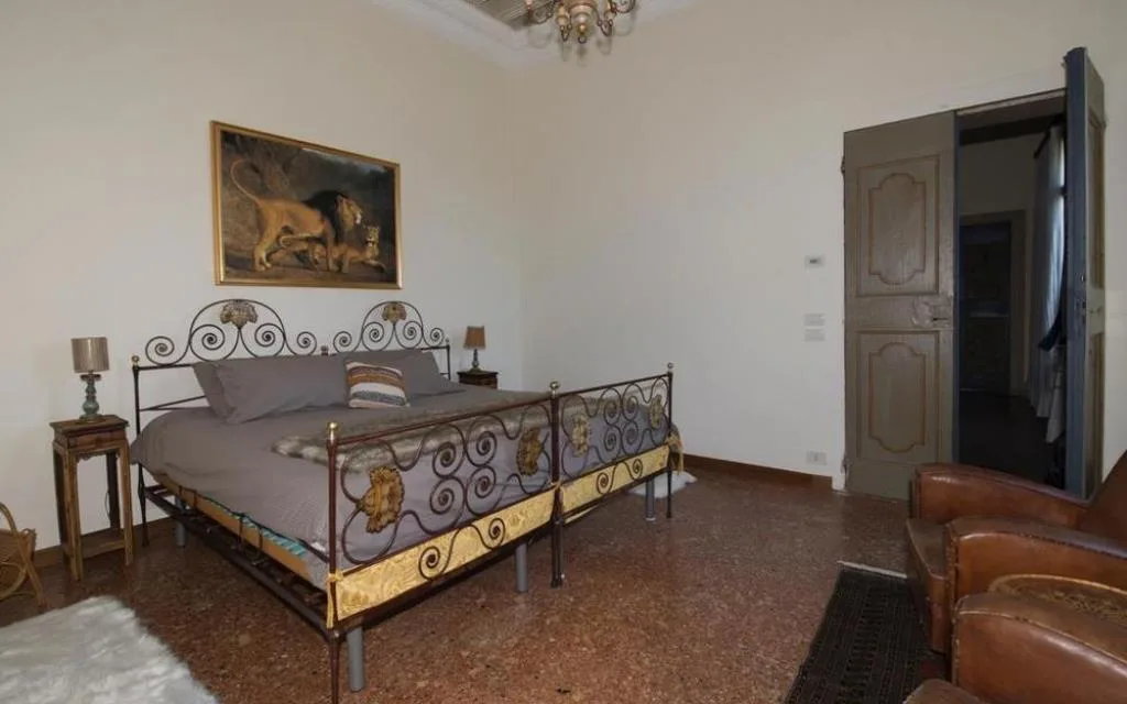 Camera con letto in ferro battuto decorato, poltrone in pelle e dipinto di leoni