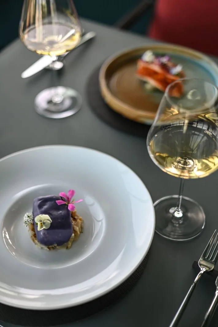 Piatto gourmet raffinato con fiori commestibili e calici di vino bianco al ristorante