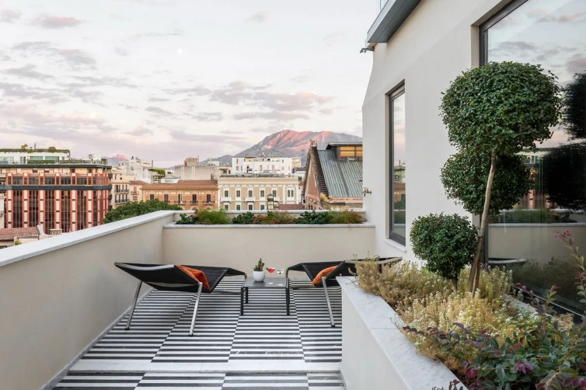 Terrazza panoramica con pavimento a scacchi, lettini e vista sui tetti e le montagne di Palermo