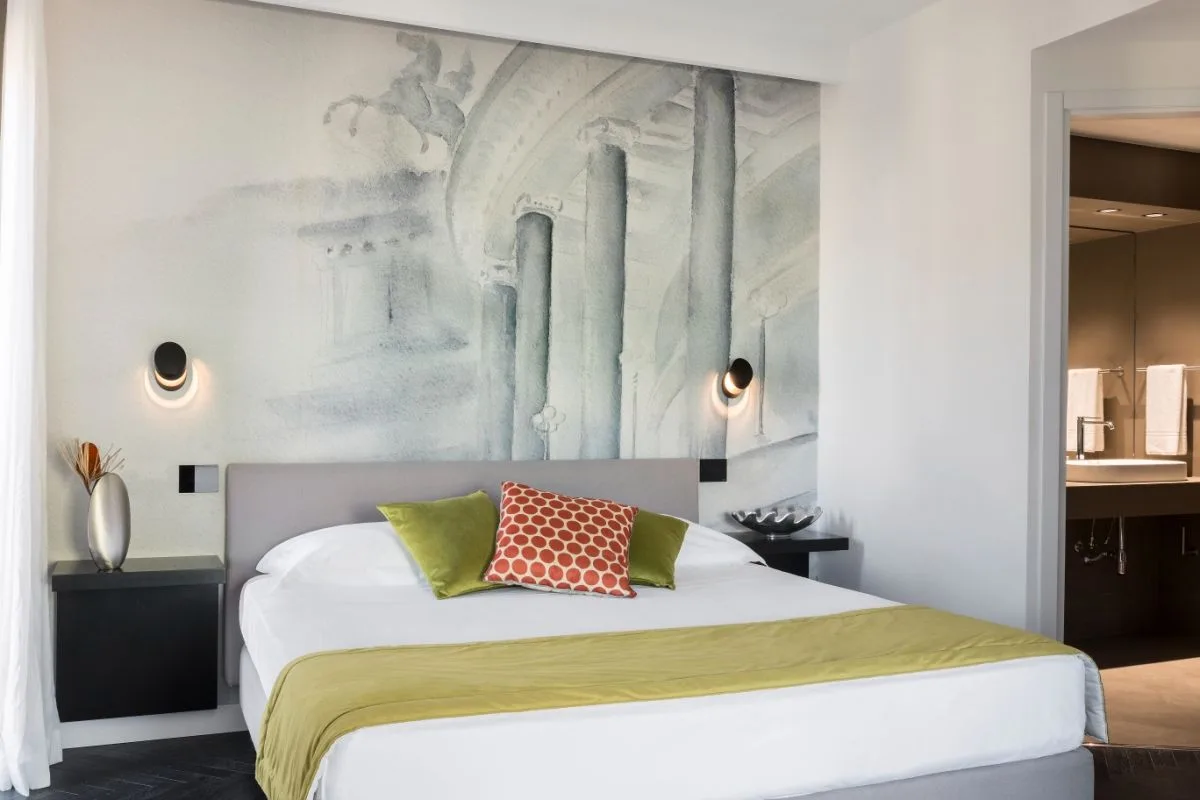 Camera elegante con murale artistico dietro il letto, cuscini colorati e bagno en-suite visibile