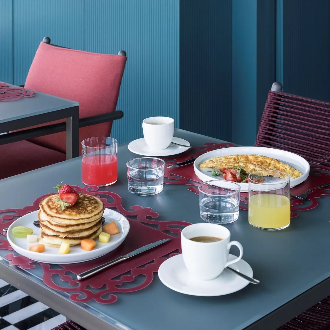 Colazione servita con pancake, frittata, caffè e succhi su tavolo con parete blu