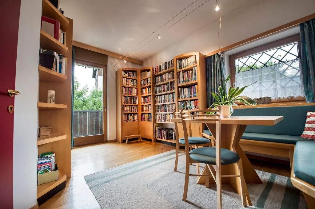 Sala lettura con libreria in legno ricca di libri, tavolo e panca verde