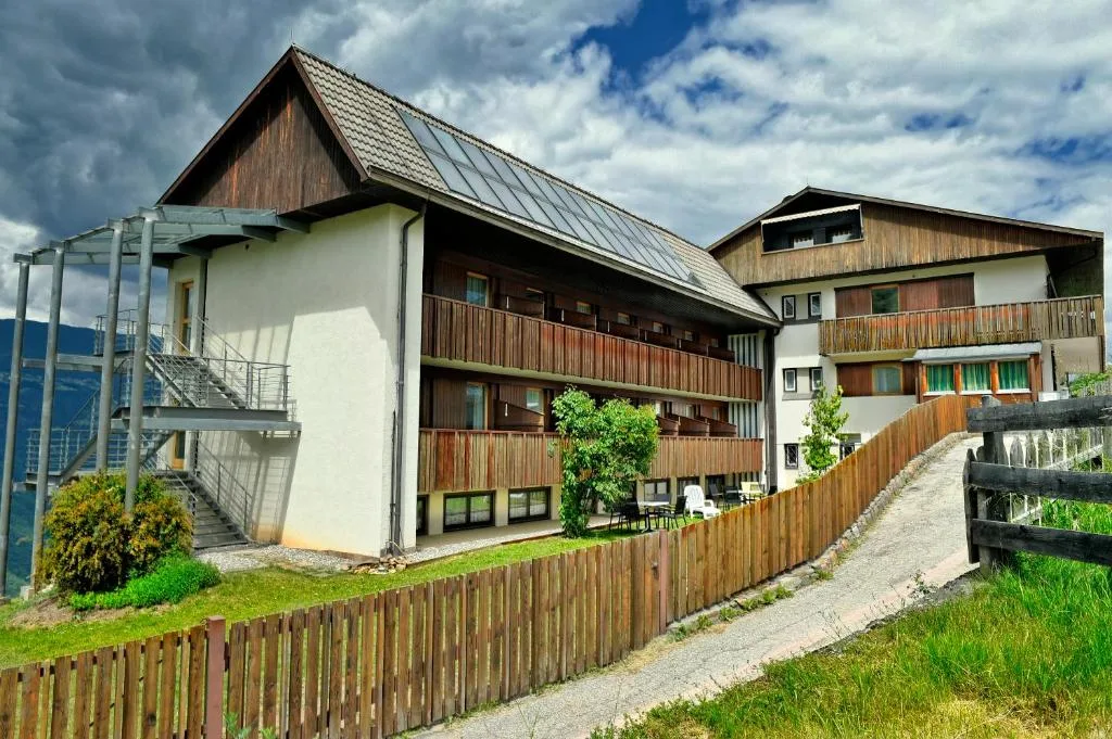 Esterno della struttura con balconi in legno, pannelli solari e cielo nuvoloso