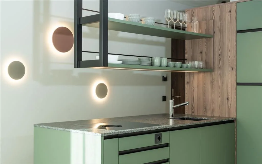 Angolo cucina verde con mensole, stoviglie e applique circolari a parete