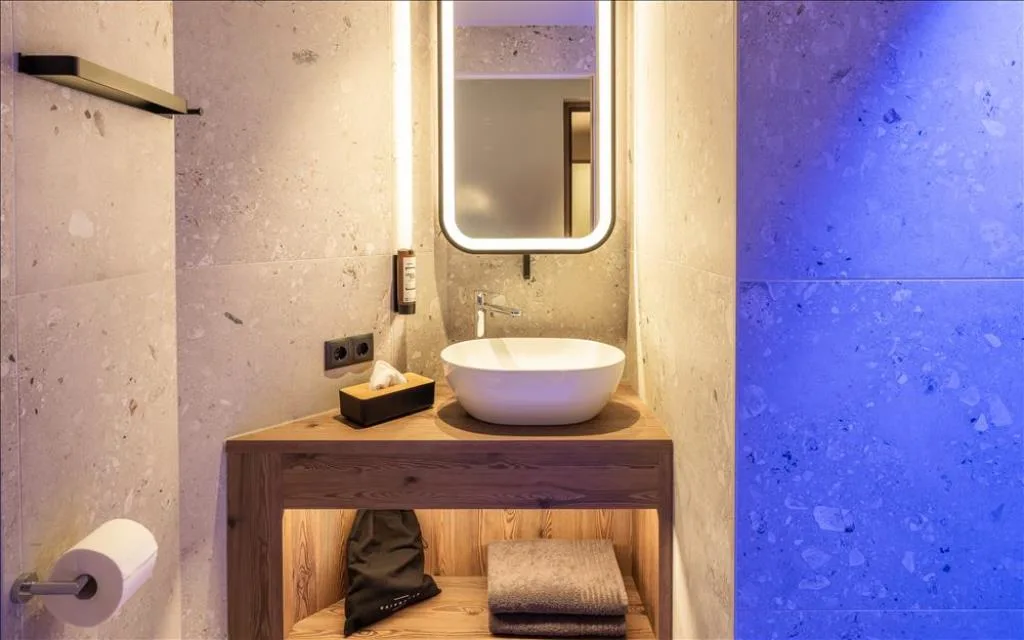 Bagno in pietra con lavabo tondo, specchio illuminato e luce blu ambientale