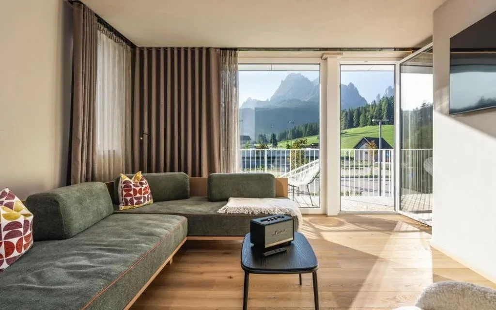Soggiorno con divano verde e ampia vetrata con vista sulle montagne