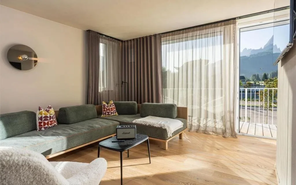 Zona living con divano angolare verde e vista panoramica alpina