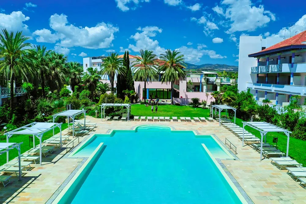 Piscina con lettini e gazebo, giardino con palme e cielo azzurro