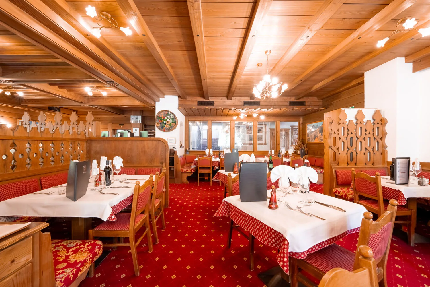 Ristorante dell'hotel con tavoli apparecchiati, moquette rossa e soffitto in legno