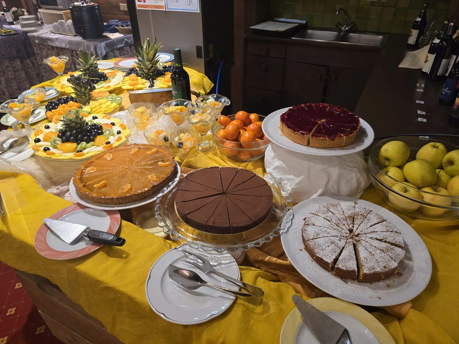 Buffet di dessert con torte, crostate e frutta esposti su tavolo giallo