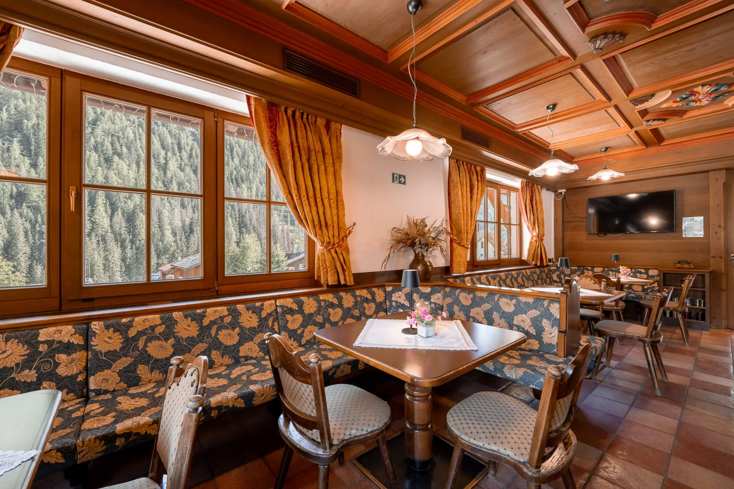 Sala colazione con panche floreali, TV e vista sul bosco dalle finestre