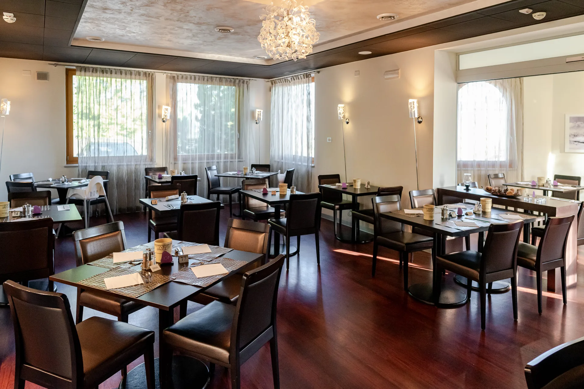 Sala ristorante con tavoli apparecchiati, sedie in legno scuro e lampadario elegante