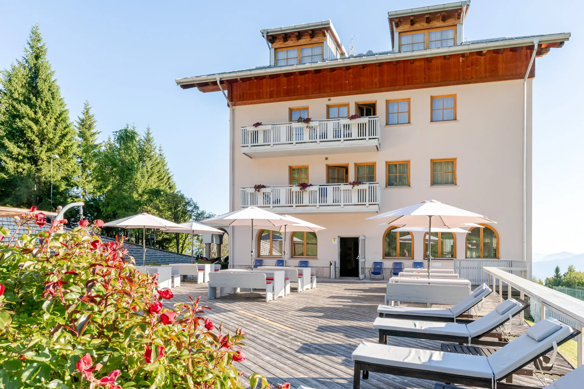 Terrazza soleggiata dell'hotel con lettini prendisole, ombrelloni e fiori rossi