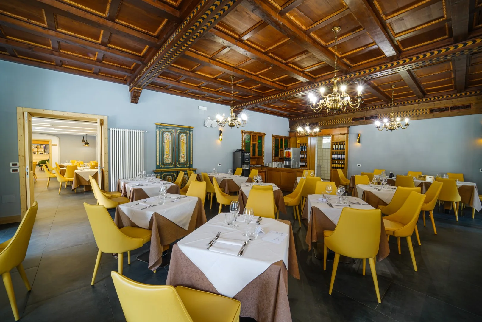 Sala ristorante con soffitto a cassettoni in legno, lampadari dorati e sedie gialle