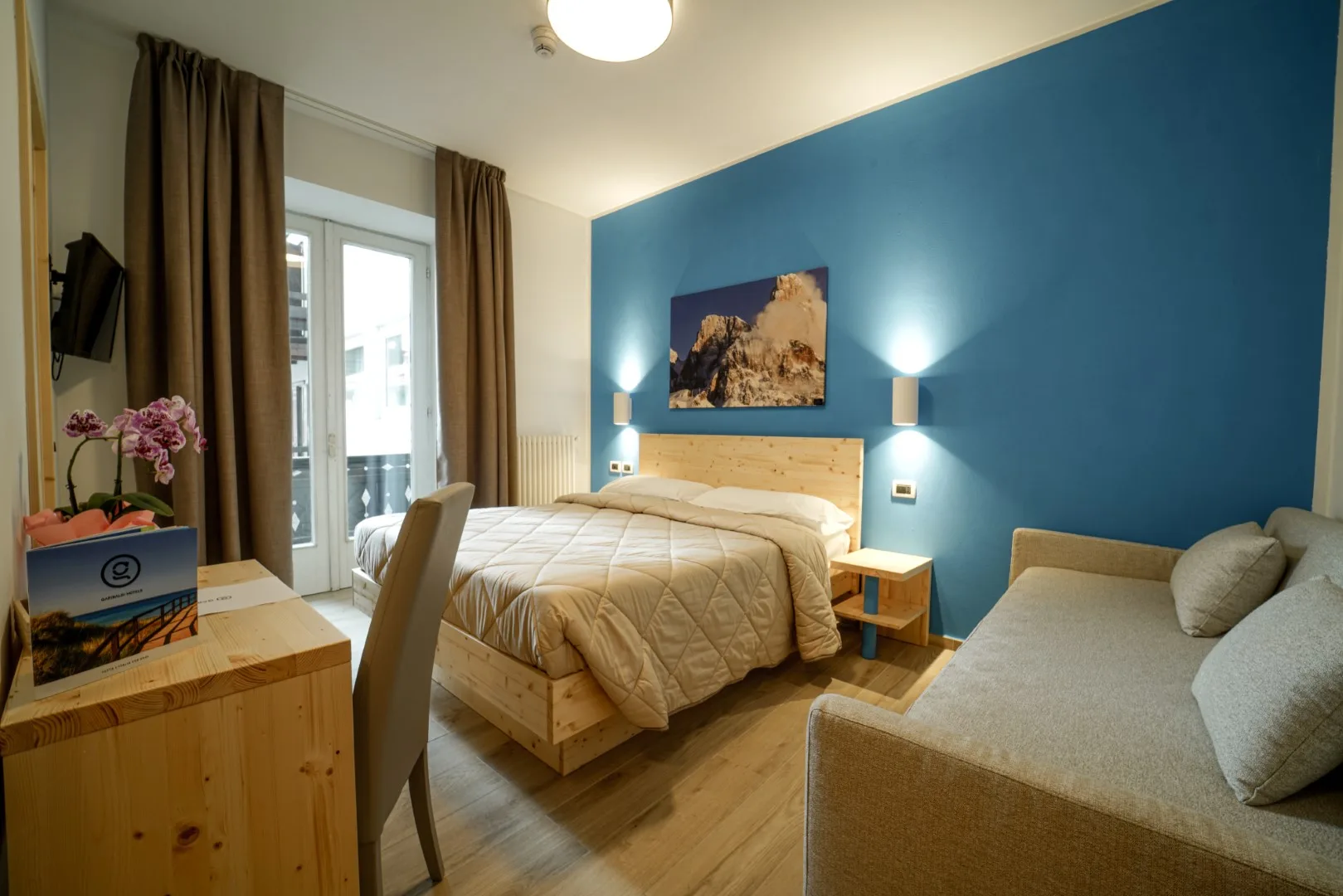 Camera matrimoniale con parete blu, arredi in legno chiaro e divano