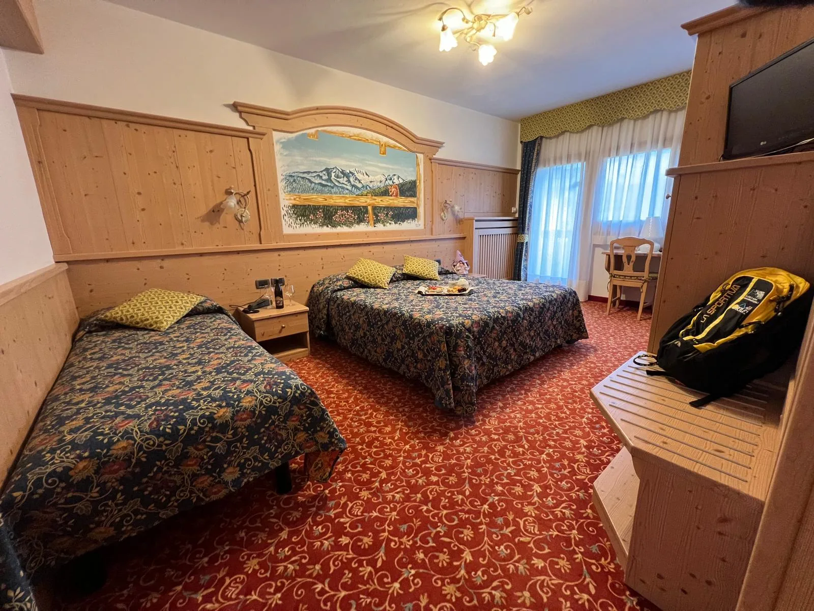 Camera in stile montano con letto matrimoniale e singolo, boiserie in legno e moquette rossa