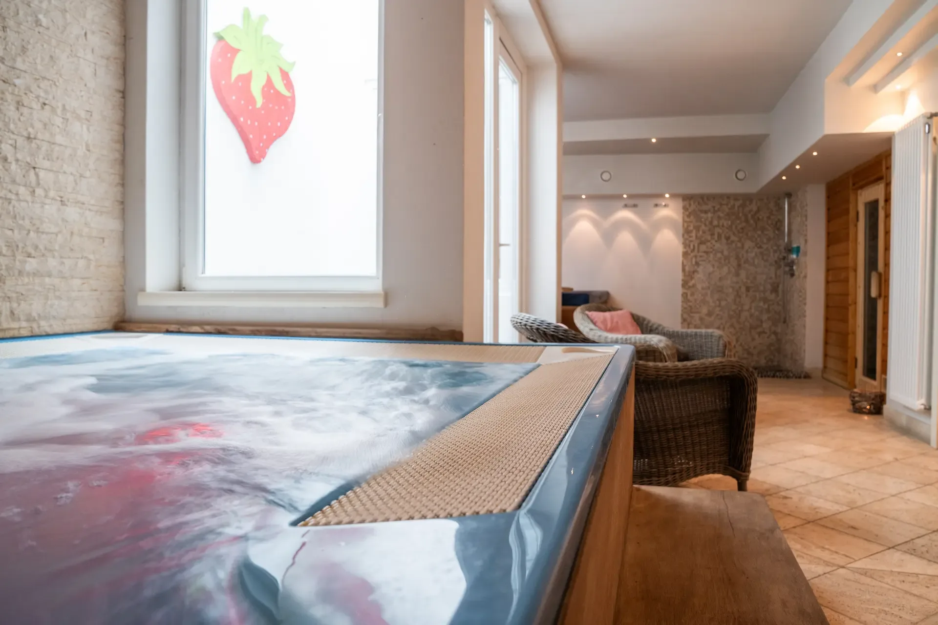 Zona relax della spa con vasca idromassaggio, poltrone in vimini e decorazione a forma di fragola