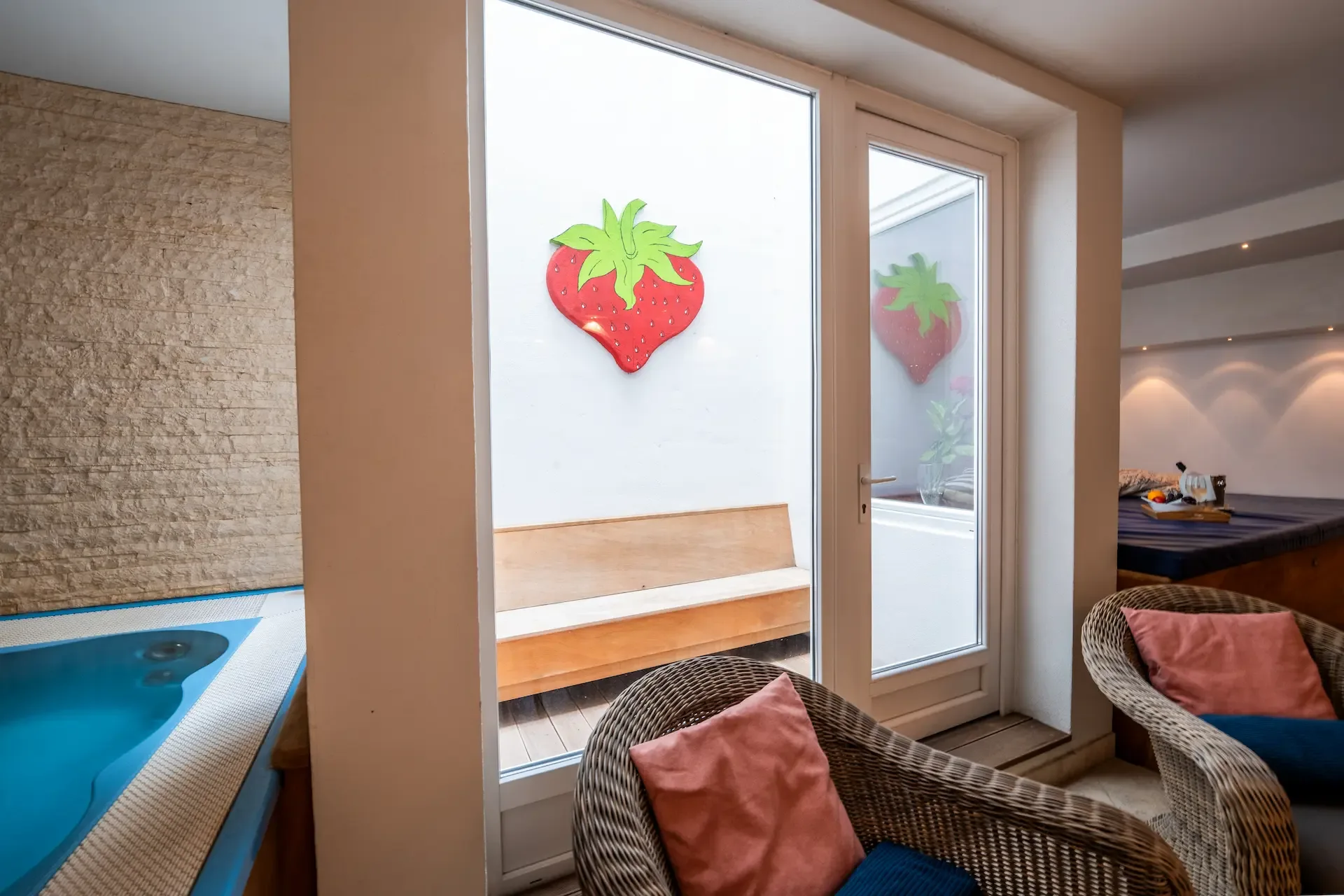 Angolo relax della spa con poltrone in vimini, cuscini e decorazioni a fragola accanto alla vasca