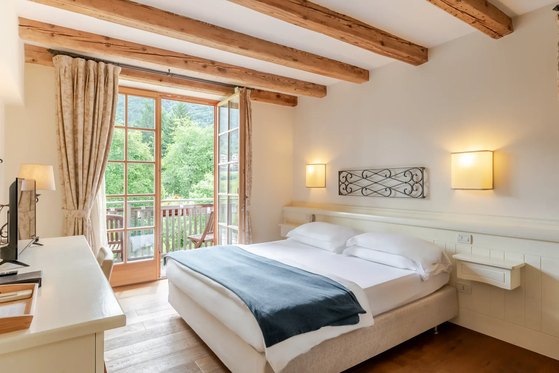 Camera da letto matrimoniale con travi a vista, balcone con vista sul verde e arredi chiari