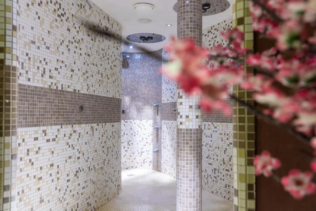 Zona docce emozionali della spa con pareti a mosaico e decorazione floreale