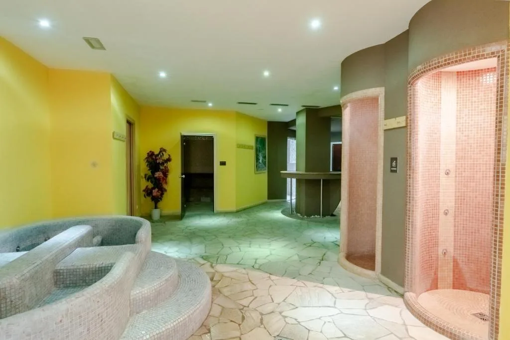 Area benessere con docce cromoterapiche, pareti gialle e pavimento in pietra