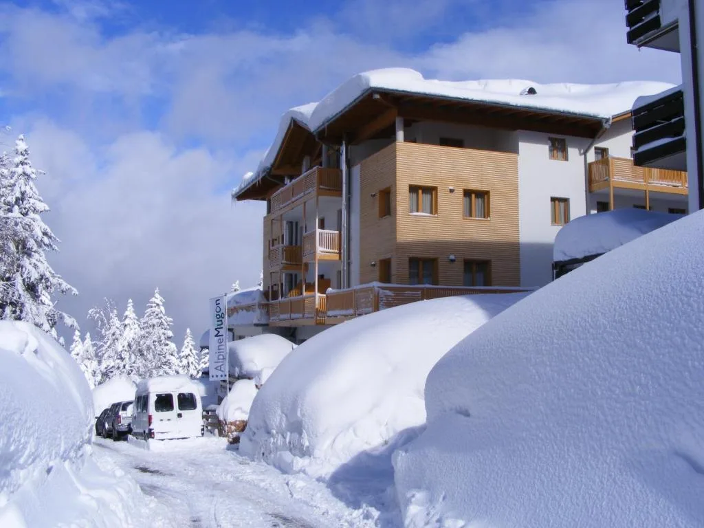 Hotel Alpine Mugon in inverno con cumuli di neve, alberi innevati e cielo azzurro