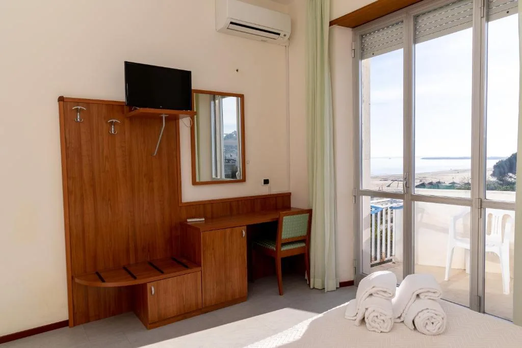 Dettaglio della camera con TV, scrivania in legno e porta finestra affacciata sul mare