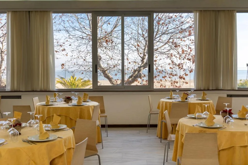 Sala ristorante con tavoli apparecchiati con tovaglie gialle e grandi finestre vista mare