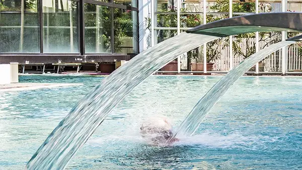Persona che si rilassa sotto una cascata d'acqua in piscina termale coperta