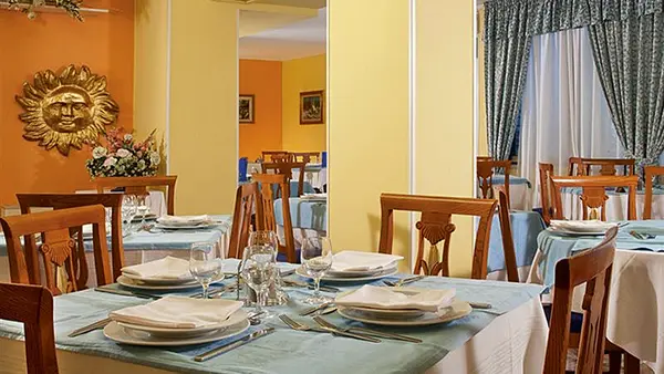Sala ristorante con tavoli apparecchiati, pareti arancioni e decorazione a forma di sole dorato